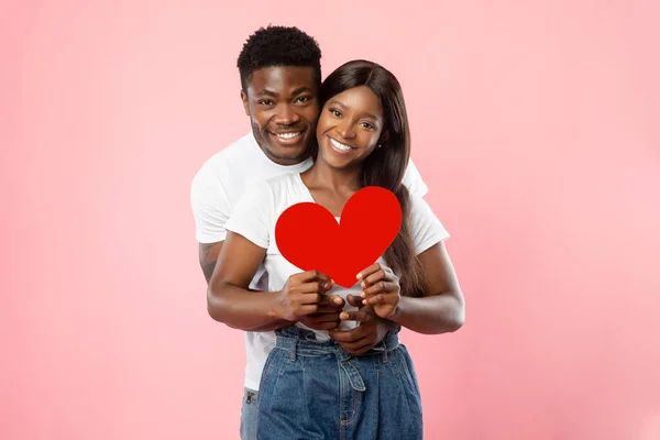 Joven pareja negra romántica abrazando y sosteniendo el corazón de papel rojo — Foto de Stock