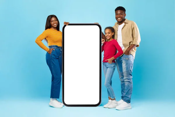 Μαύρη οικογένεια δείχνει λευκό άδειο smartphone ακουμπά στη μεγάλη οθόνη — Φωτογραφία Αρχείου