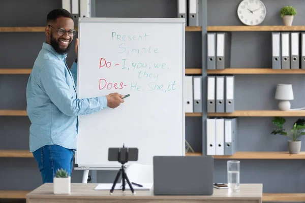 Ευτυχισμένη χιλιετή ελκυστική μαύρος δάσκαλος δείχνει τους αγγλικούς κανόνες στον πίνακα, κοιτάζει το τηλέφωνο — Φωτογραφία Αρχείου