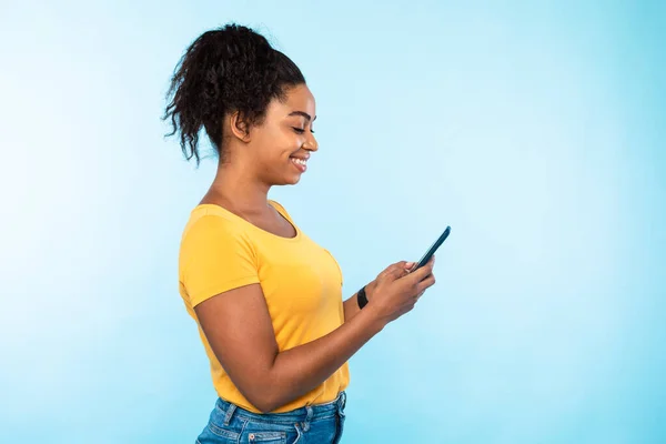 쾌활하고 젊은 흑인 여성은 스마트폰을 사용하고, 친구와 온라인 대화를 나누고, 인터넷 서핑을 하고, 비디오를 보고, 빈 공간을 사용 한다. — 스톡 사진