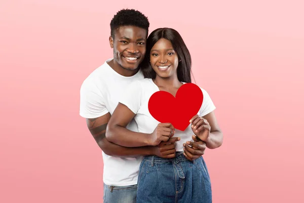 若いロマンチックな黒のカップルの抱擁と保持レッドペーパーハート — ストック写真