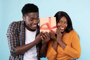 Mutlu siyah çift mavi stüdyoda hediye kutusunu sallıyor.