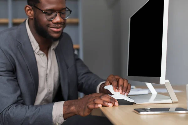 Millennial black businessman sitting ar desk with pc monitor, wiping computer mouse with sanitizer at office, mockup — Fotografia de Stock