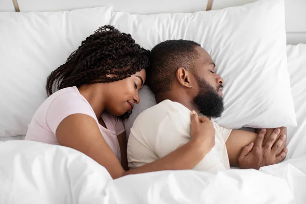Millennial black female and male lie on bed, sleep, hugging on soft pillow, under white blanket in bedroom, close up — ストック写真