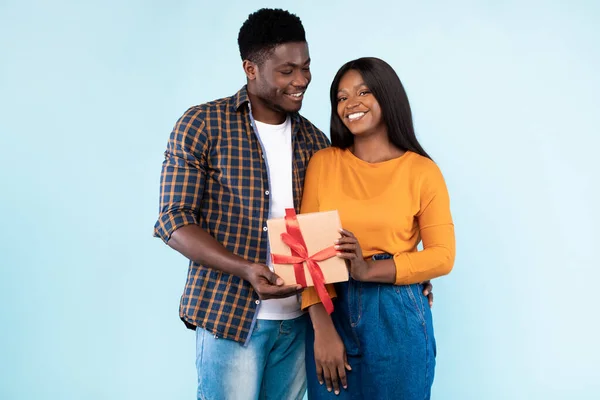 Happy black couple holding gift box at blue studio — Stockfoto