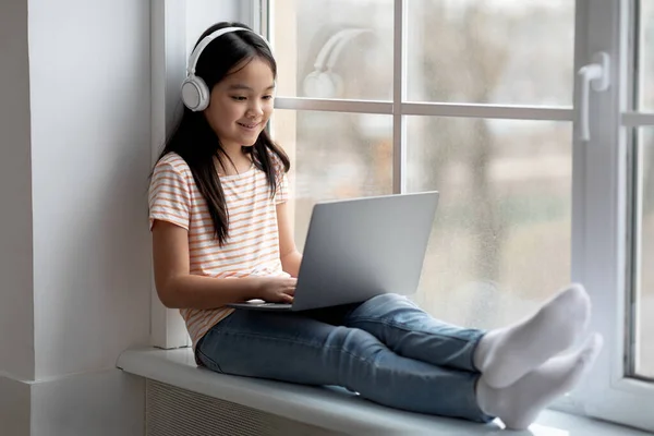 Cheerful little korean girl with wireless headset using laptop — Fotografia de Stock