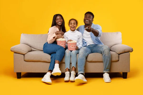 Happy young family watching television with popcorn sitting on sofa — Stockfoto
