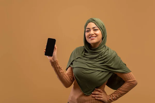 Saya merekomendasikan aplikasi ini. Wanita arab yang bersemangat memegang smartphone dengan layar kosong hitam di tangan dan tersenyum, mockup — Stok Foto