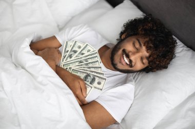 Neşeli Hintli adam uyurken dolarlara sarılıyor.