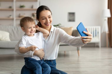 Genç mutlu anne, küçük oğluyla selfie çekiyor, evde birlikte vakit geçiriyorlar.