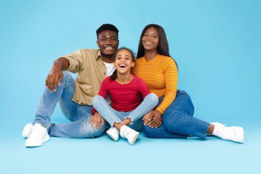Afrikalı Amerikalı kız gülümseyen anne ve babasıyla poz veriyor.