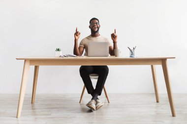 Milenyum siyahi ofis çalışanı yaratıcı fikirlere sahip, iş yerinde Eureka 'yı işaret eden, beyaz duvara karşı masada oturan