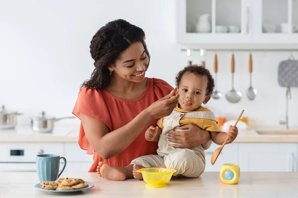 Baby Weaning. Caring Black Mother Feeding Toddler Son From Spoon In Kitchen — Stockfoto