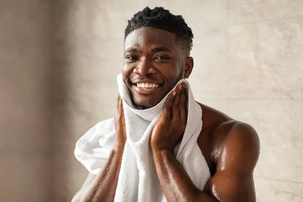 Щасливий чорний хлопець витирає обличчя з м'яким рушником у ванній — стокове фото