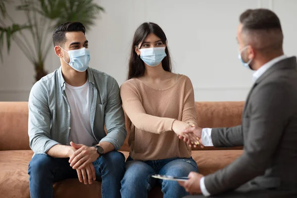 Pareja feliz en mascarillas estrechando la mano con el terapeuta en la oficina —  Fotos de Stock