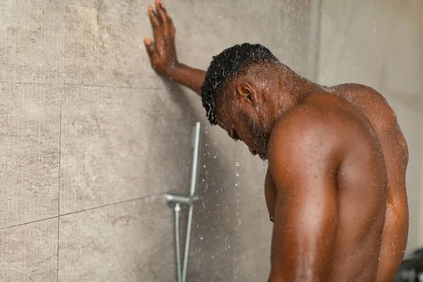 Siyah adam duş alıyor. Suyun altında duruyor. Banyoda dinleniyor.