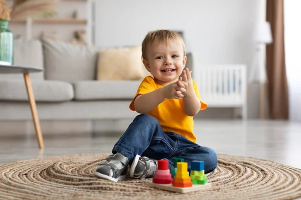 Adorable toddler boy playing with educational wooden toy at home, clapping hands and smiling, sitting on carpet — Stock fotografie