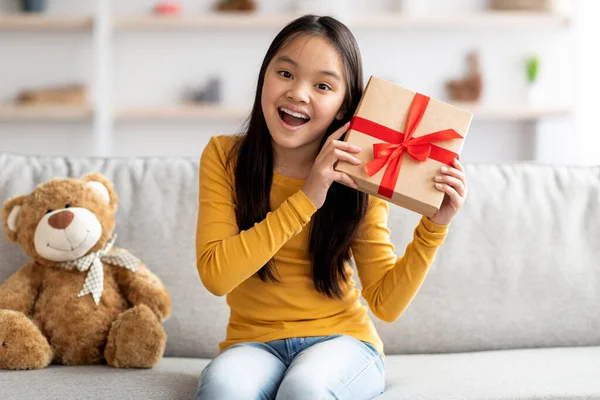 Little asian girl holding red gift box in living room — Fotografia de Stock