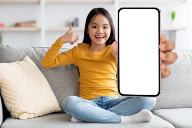 Neşeli Asyalı çocuk cep telefonunu boş ekranla gösteriyor.