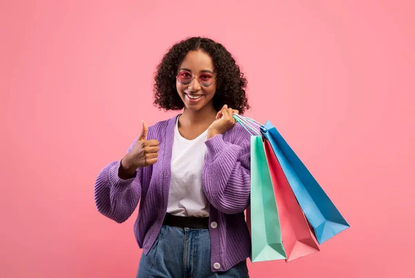 Great shopping. Happy young black woman gesturing thumbs up, holding shopper bag, recommending great sale — ストック写真