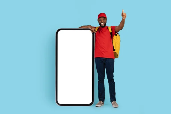 Happy African American Delivery Guy With Thermal Backpack Standing Near Blank Smartphone — 图库照片