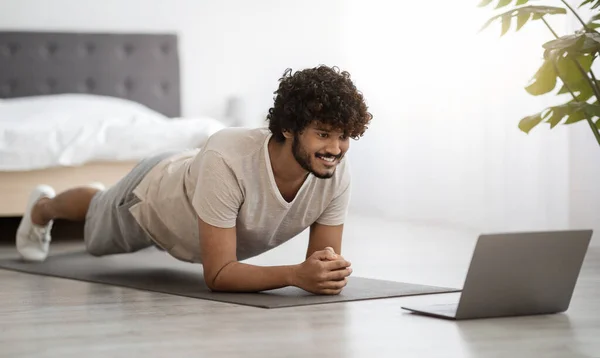 Happy athletic hindu man planking at home, using computer — Foto Stock