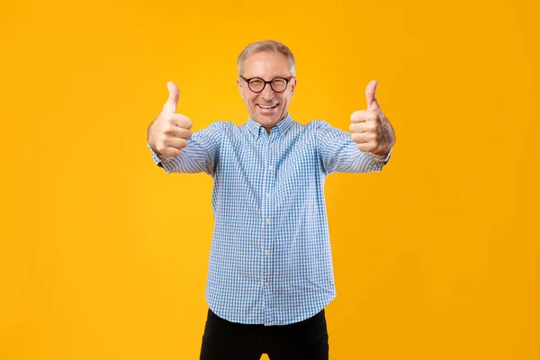 Happy mature guy gesturing thumbs up and smiling at studio — Stock Fotó