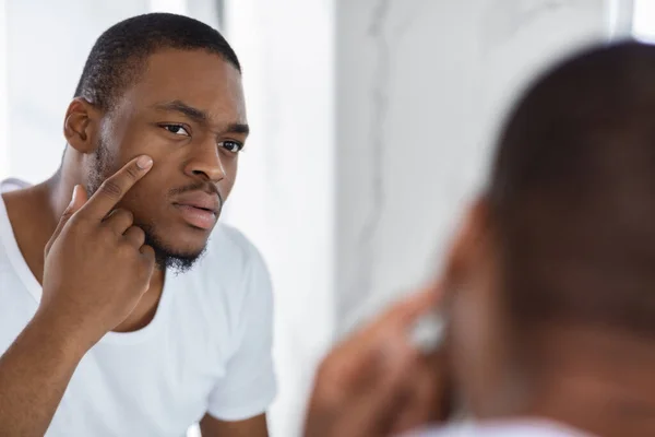 Preocupado joven negro examinando su cara mientras mira el espejo — Foto de Stock