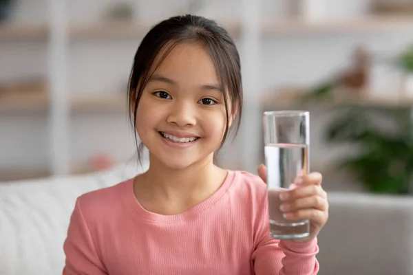 Smiling little girl with glass of water at home – stockfoto