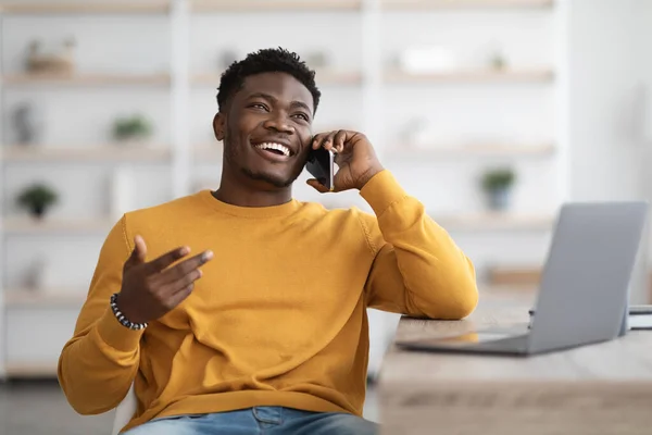 Smiling man sitting at table with laptop, having phone conversation — Stockfoto