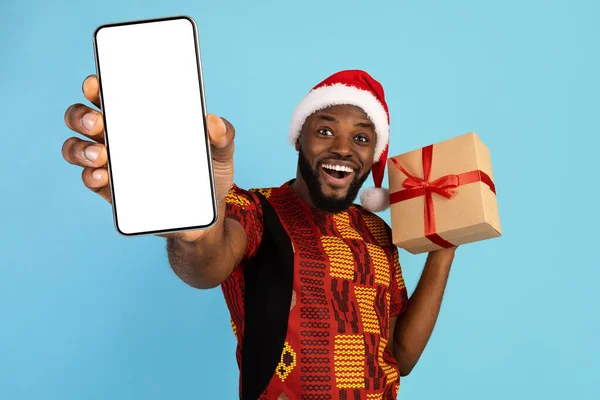 Black Man In Santa Hat Holding Christmas Gift And Showing Blank Smartphone — Photo