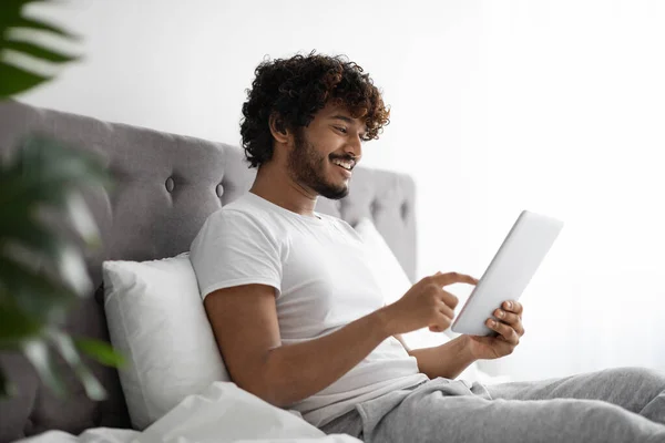 快乐的印度年轻人在床上用数码平板电脑 — 图库照片