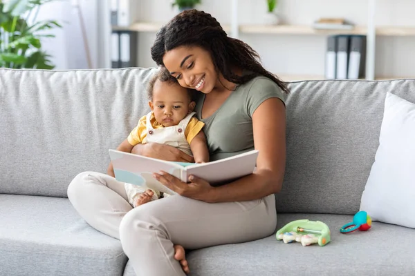 Spending Time With Baby. Loving Black Mother Reading Book To Infant Child — стоковое фото