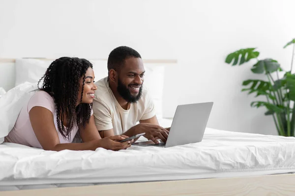 Gelukkig jong zwart man en vrouw liggen op bed en bekijk video op computer in vrije tijd — Stockfoto