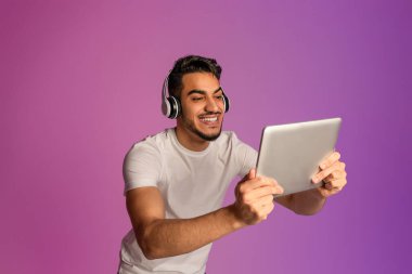 Kulaklık takan yakışıklı genç bir Arap, tablet ekrana bakıyor, neon ışıkta modern bir alet kullanıyor.