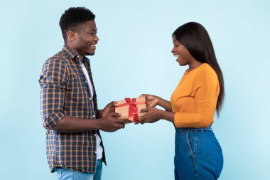 Happy black couple holding giving gift box at blue studio
