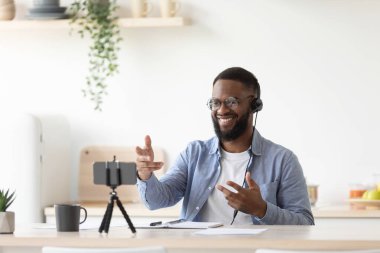 Glad millennial african american man teacher with beard in glasses and headphones gestures with hands