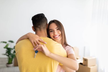 Mortgage and relocation concept. Happy Caucasian lady hugging her boyfriend, holding key from new house