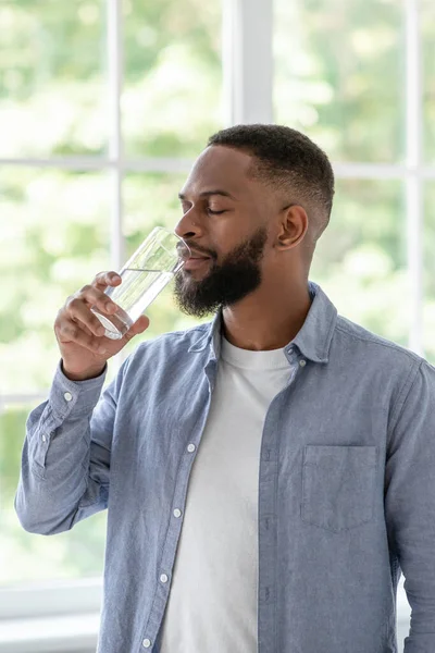 Millennial african american guy with beard and perfect skin drinks clean water from glass with closed eyes — Fotografia de Stock
