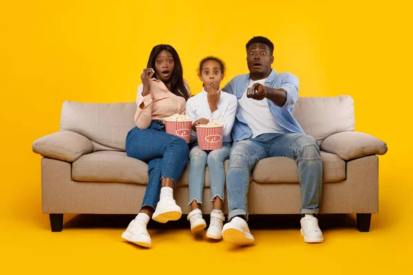 Surprised young family watching television with popcorn sitting on sofa — Fotografia de Stock