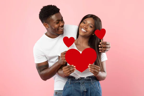 Joven pareja negra romántica posando y sosteniendo corazones de papel rojo — Foto de Stock