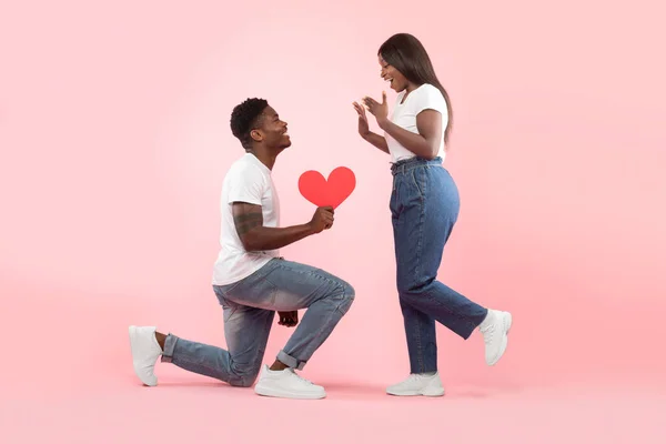 Black man holding red paper heart standing on one knee — Stockfoto