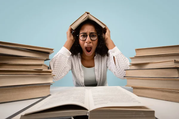 Furious young black woman putting book on her head and screaming on blue studio background — Stockfoto