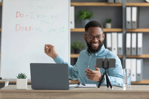Sonriente guapo joven negro tutor masculino con barba mostrar reglas de Inglés y mira a la PC y teléfono inteligente —  Fotos de Stock
