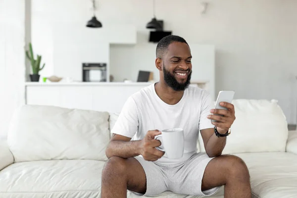 Hombre negro usando su smartphone bebiendo café — Foto de Stock