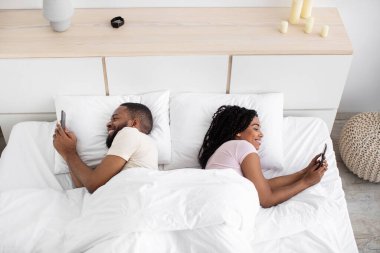 Cheerful glad young black lady and guy suffer from addiction to phone, social networks and online games
