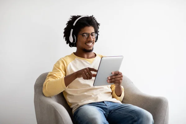 Young Black Guy In Wireless Headphones Relaxing With Digital Tablet In Armchair —  Fotos de Stock