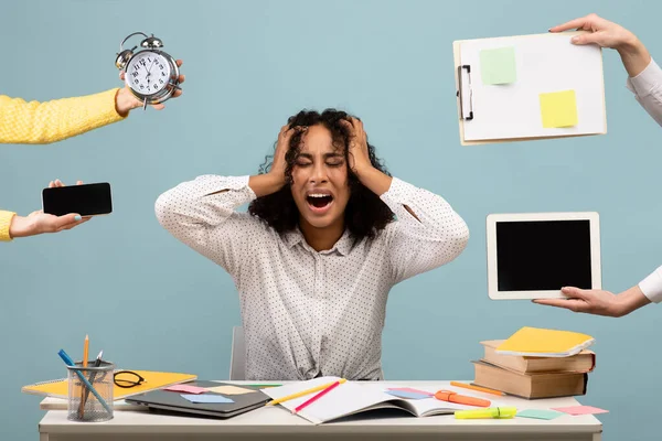 Black lady sitting at desk surrounded by hands with clock and gadgets, screaming in despair, suffering from burnout — стоковое фото