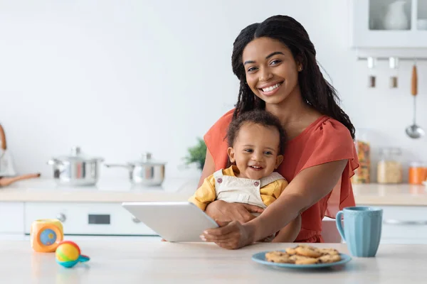 Beautiful Young Black Mom And Infant Child Using Digital Tablet In Kitchen — стоковое фото