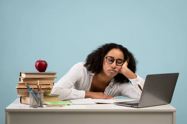 Education and overworking. Tired black female student studying at desk with laptop against blue studio background —  Fotos de Stock